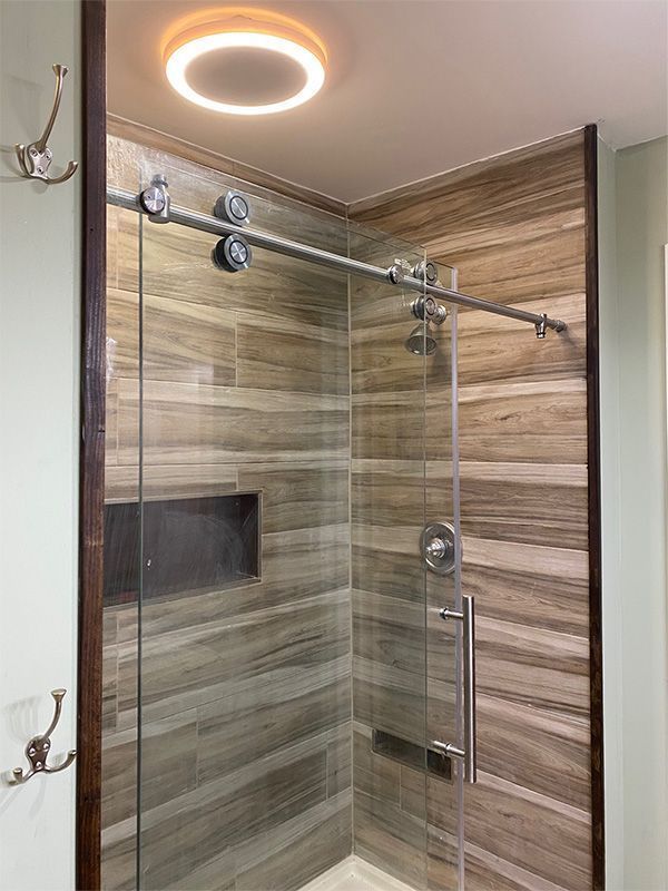Modern glass shower with wood-look tile walls and a round ceiling light