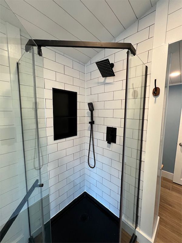 Modern tiled shower with black floor, glass door, rain showerhead, and handheld sprayer