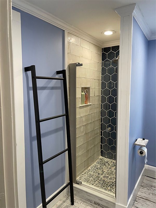 Blue bathroom with white-tiled shower, hex-pattern accent wall, and black ladder-style towel rack