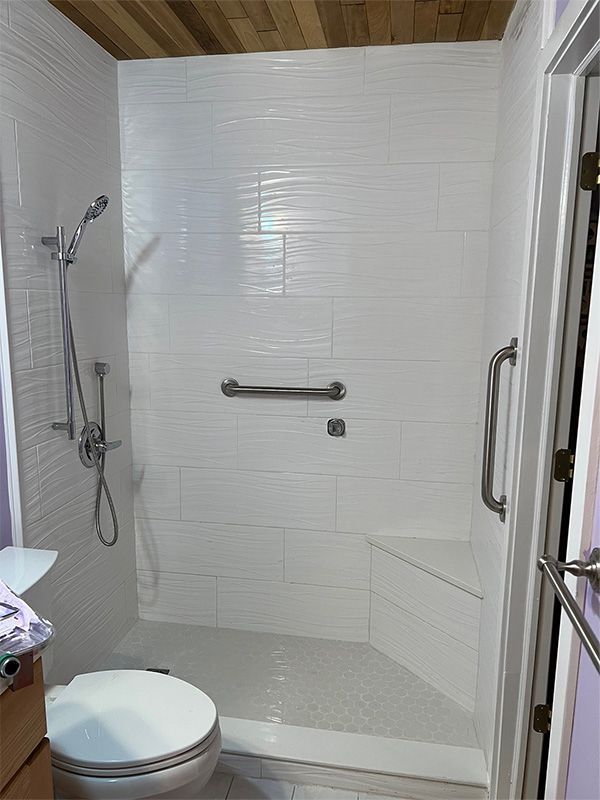 Accessible walk-in shower with white tile walls, grab bars, showerhead, and built-in bench in a bathroom