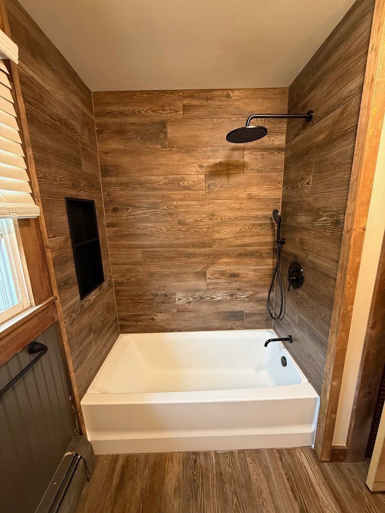 Small rustic bathroom with wood walls, white tub, and black shower fixtures