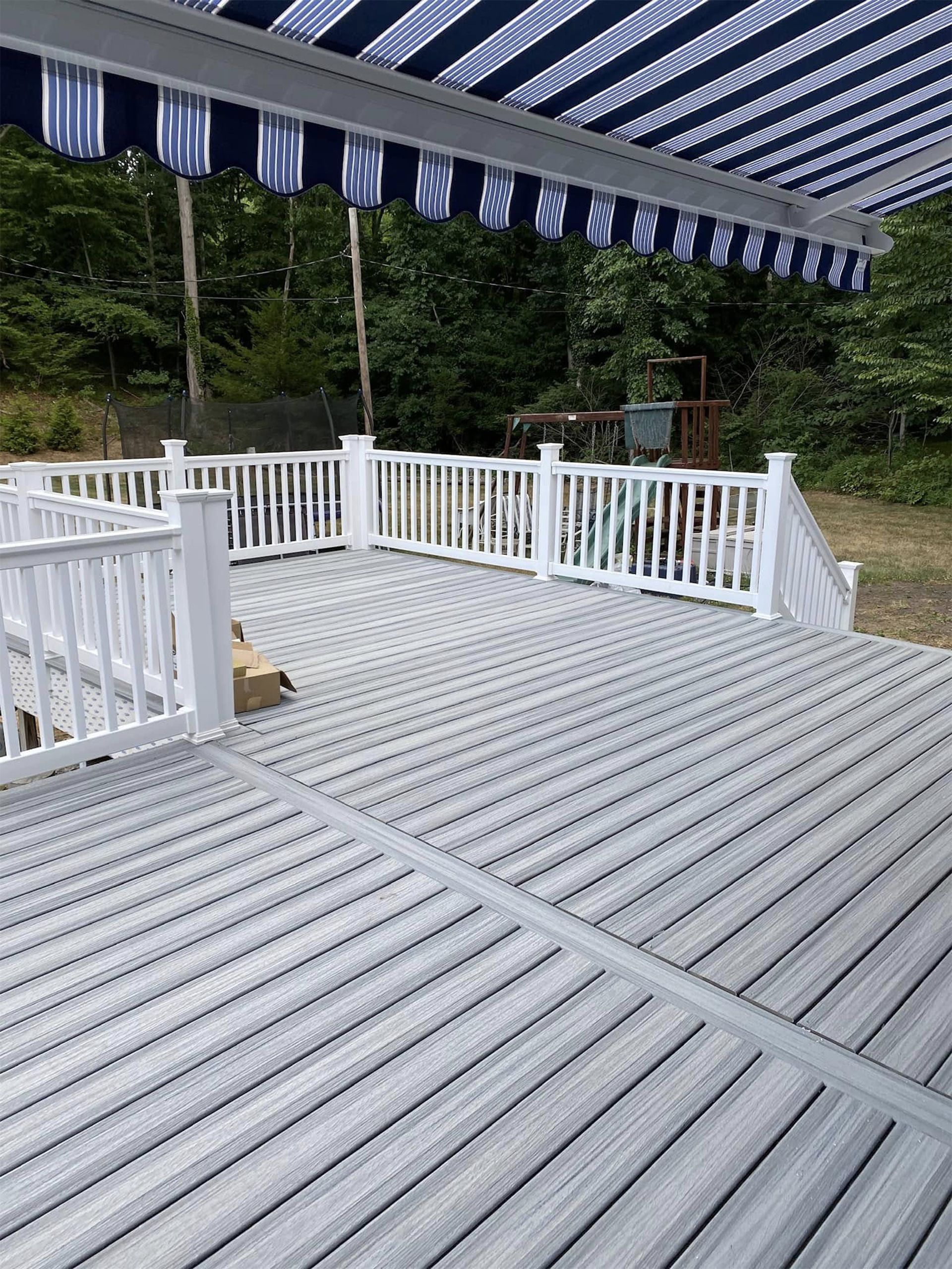 White deck with railings under a striped awning, overlooking trees and greenery outdoors