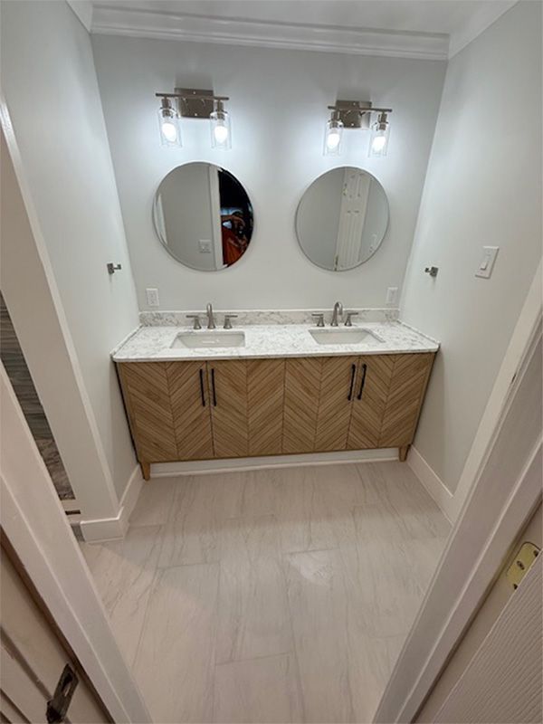 Modern bathroom vanity with two round mirrors, double sinks, and wood cabinets in a white tiled room