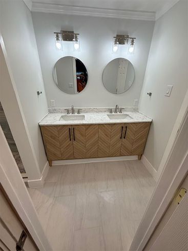Modern bathroom vanity with dual sinks, round mirrors, and wood cabinets under wall sconces
