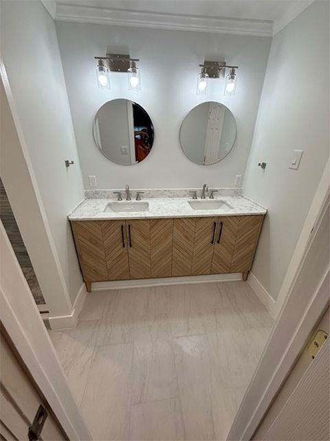 Modern bathroom vanity with dual sinks, round mirrors, and wood cabinets under wall sconces