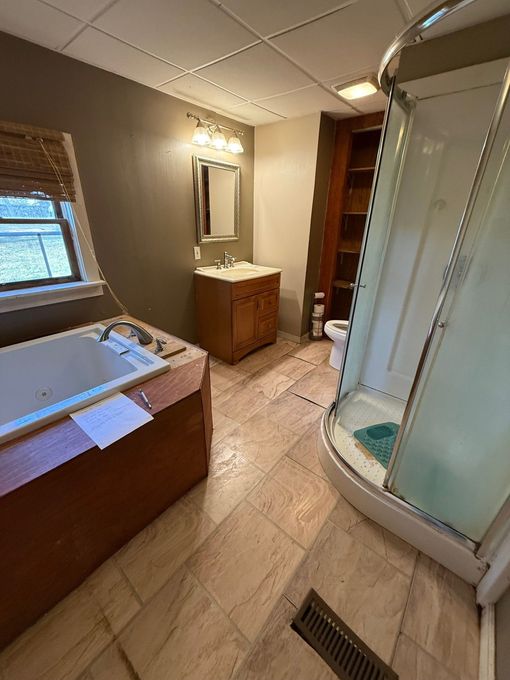 Bathroom with tub, vanity, mirror, and glass shower stall on beige tile floor.
