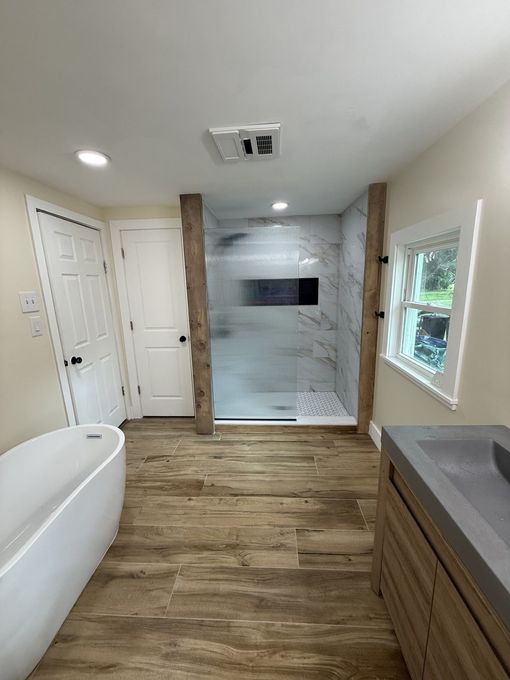Modern bathroom with freestanding tub, wood floors, double vanity, and a tiled walk-in shower