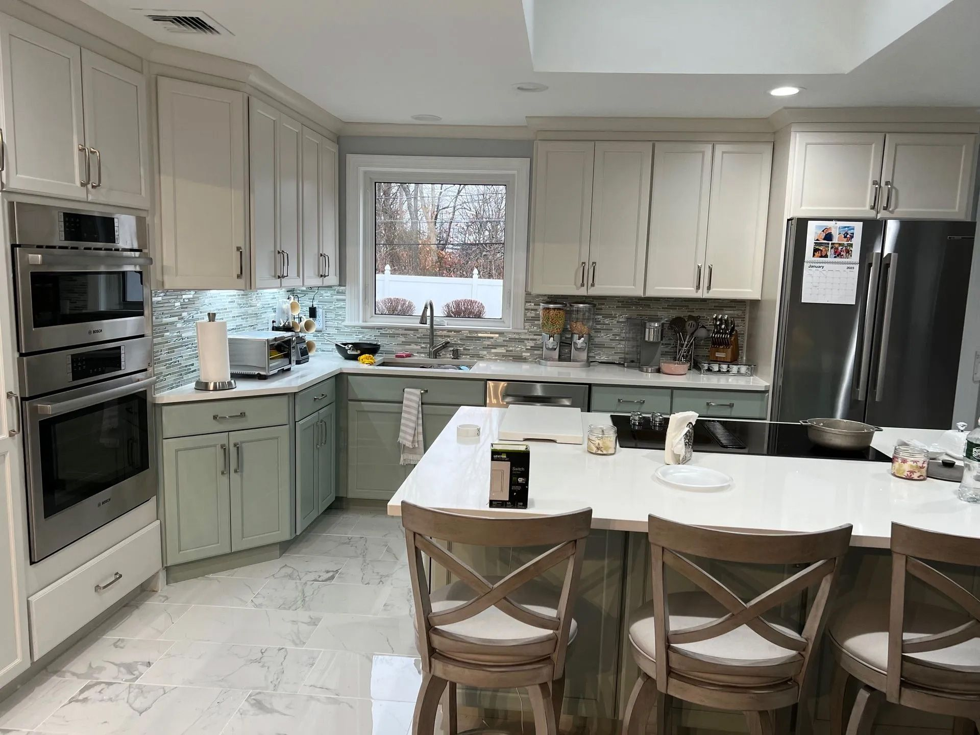 Bright white kitchen with island, green lower cabinets, and large window over the sink.