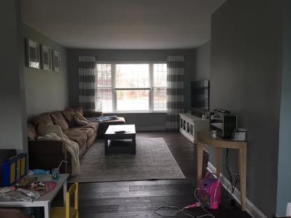 Living room with gray walls, brown sofa, coffee table, large window, and a TV stand along the right wall