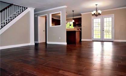 Empty modern living room with dark hardwood floors, gray walls, staircase, and French doors to a patio
