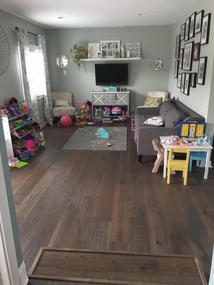 Living room with dark wood floors, gray walls, TV, shelves, toys, and a small table by a couch