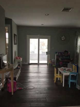 Living room with dark wood floor, sliding glass doors, and children’s play furniture on the right