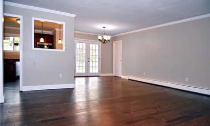 Empty living room with dark hardwood floors, gray walls, French doors, and a pass-through opening to the kitchen