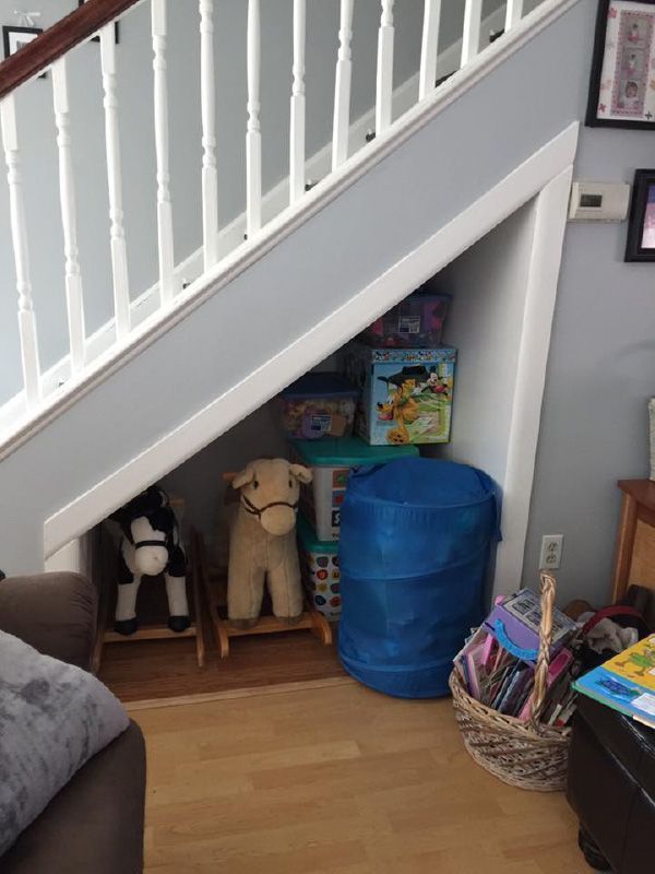 Storage nook under staircase with toys, stuffed animals, and a blue bin on a wood floor
