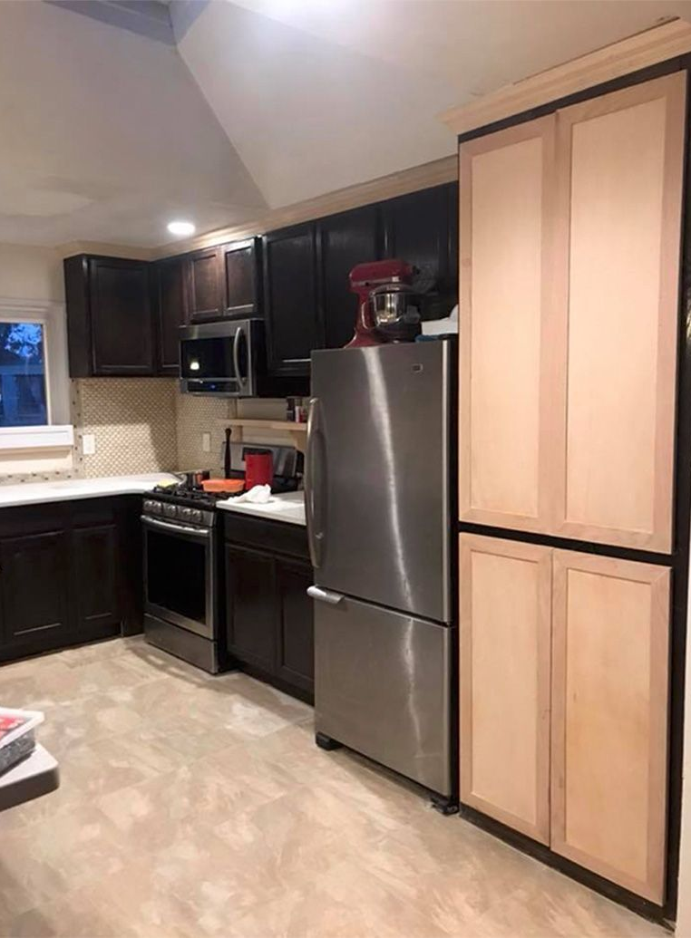 Kitchen with black cabinets, stainless steel refrigerator and stove, light countertops, and tall pantry cabinets.