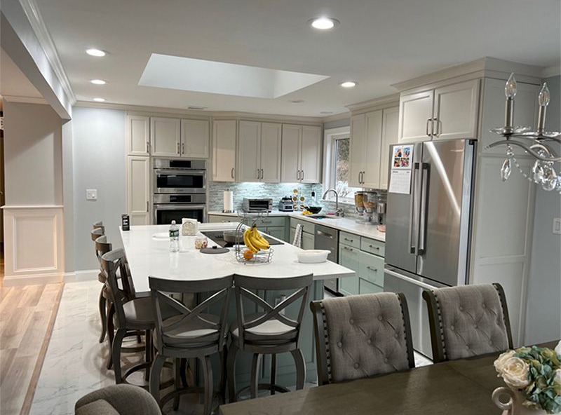 Bright modern kitchen with white cabinets, stainless appliances, island, and dining table under recessed lights