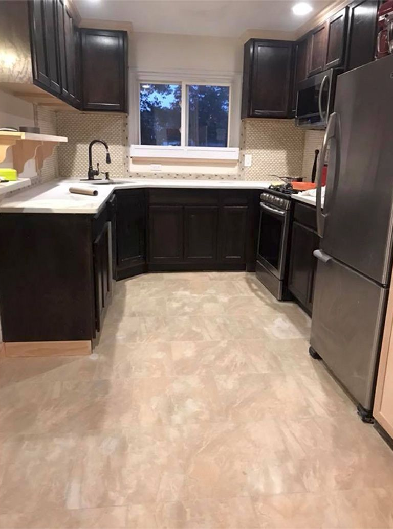 Small kitchen with dark cabinets, stainless refrigerator, stove, sink, and a window over the counter.