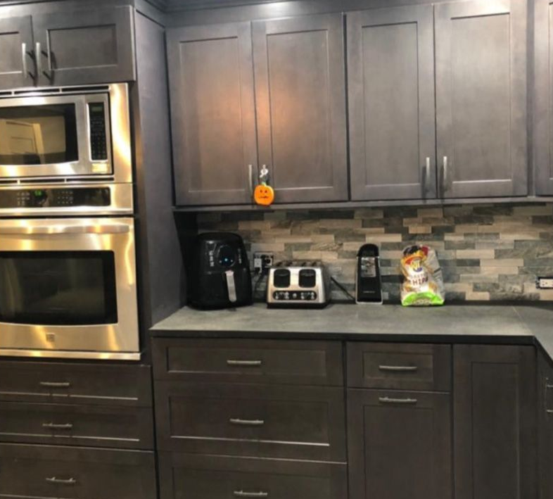 Modern kitchen with dark wood cabinets, stainless steel oven, and countertop appliances against a tiled backsplash