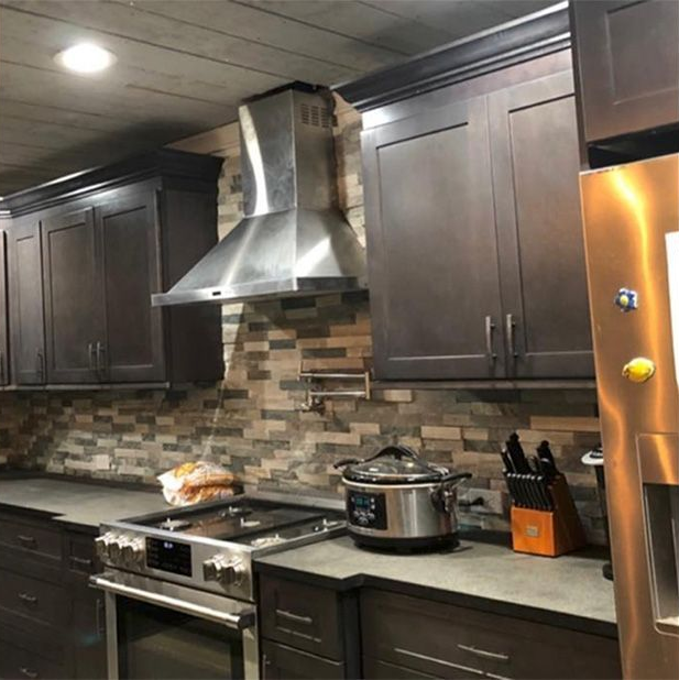 Modern kitchen with dark cabinets, stainless steel range hood, stove, countertop, and slow cooker