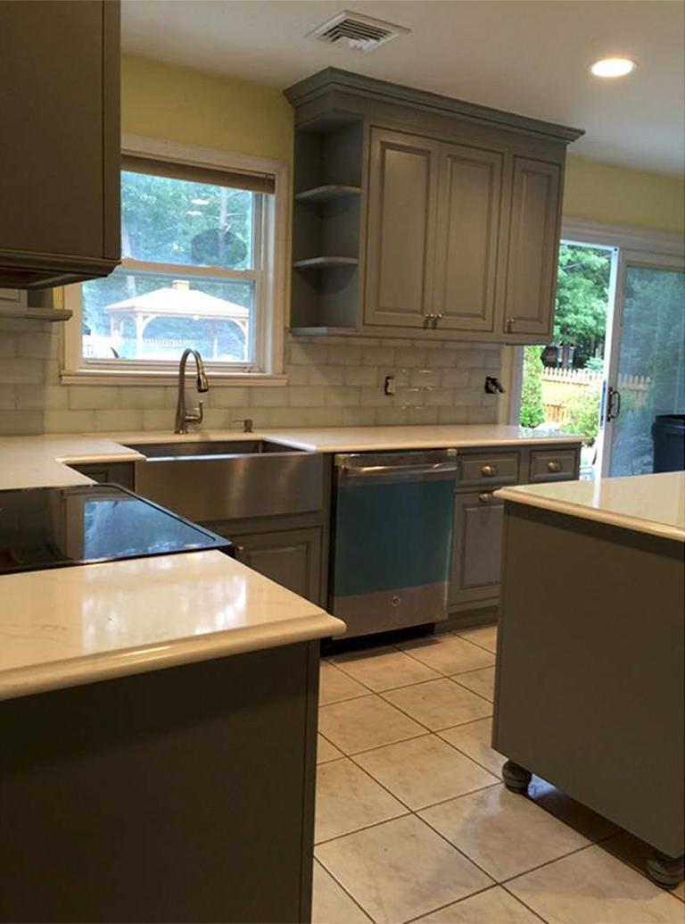 Modern kitchen with gray cabinets, tiled floor, sink under a window, and a central island.