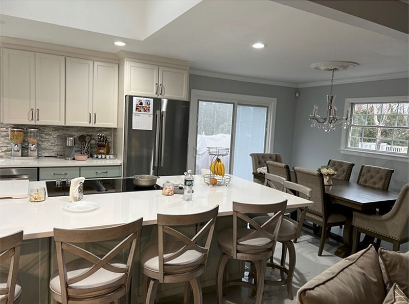 Bright kitchen and dining area with white cabinets, island, chairs, and large windows