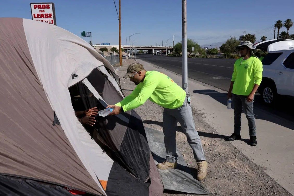 Two men are standing next to a tent on the side of the road.