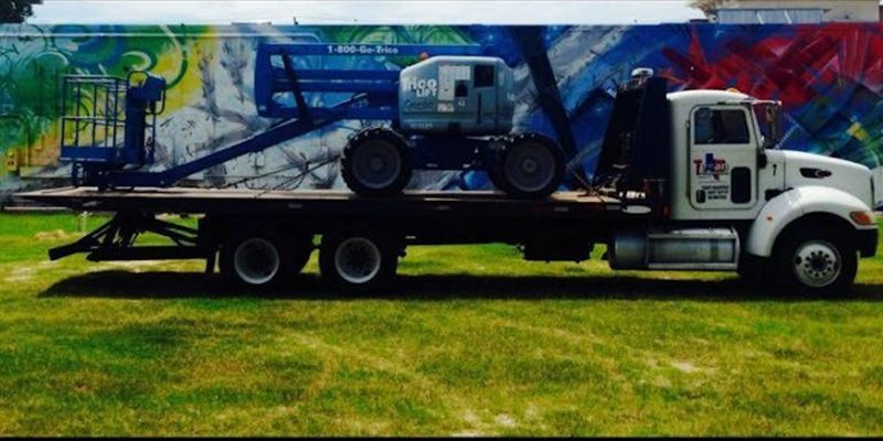 White tow truck hauling a blue graffiti-covered car on a flatbed, parked on grass
