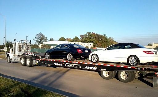 Two cars on a flatbed trailer being towed along a road in daylight