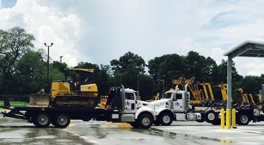 White tow truck with yellow heavy equipment parked in a wet lot under cloudy skies