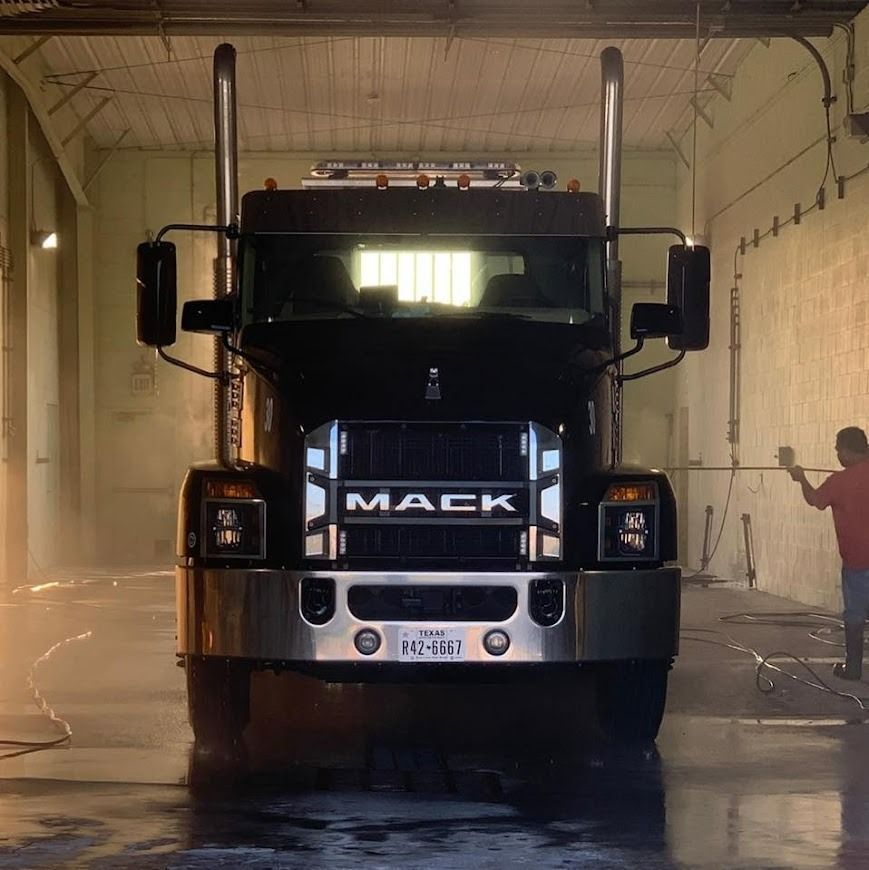 Black Mack truck parked indoors in a dim garage, front view with headlights glowing.