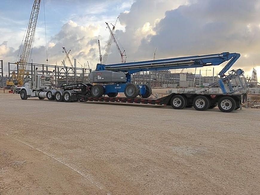 Large blue crane on a multi-axle trailer at a construction site under cloudy sky