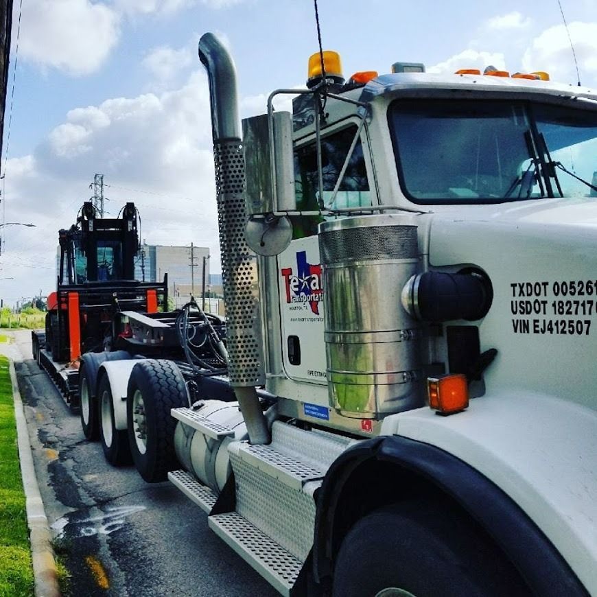 White semi truck parked on roadside with a black forklift loaded behind it under a cloudy sky