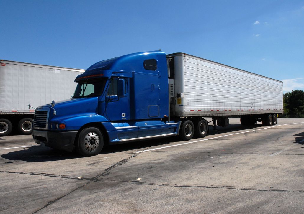 Blue semi-truck with silver trailer parked in a lot under a clear sky
