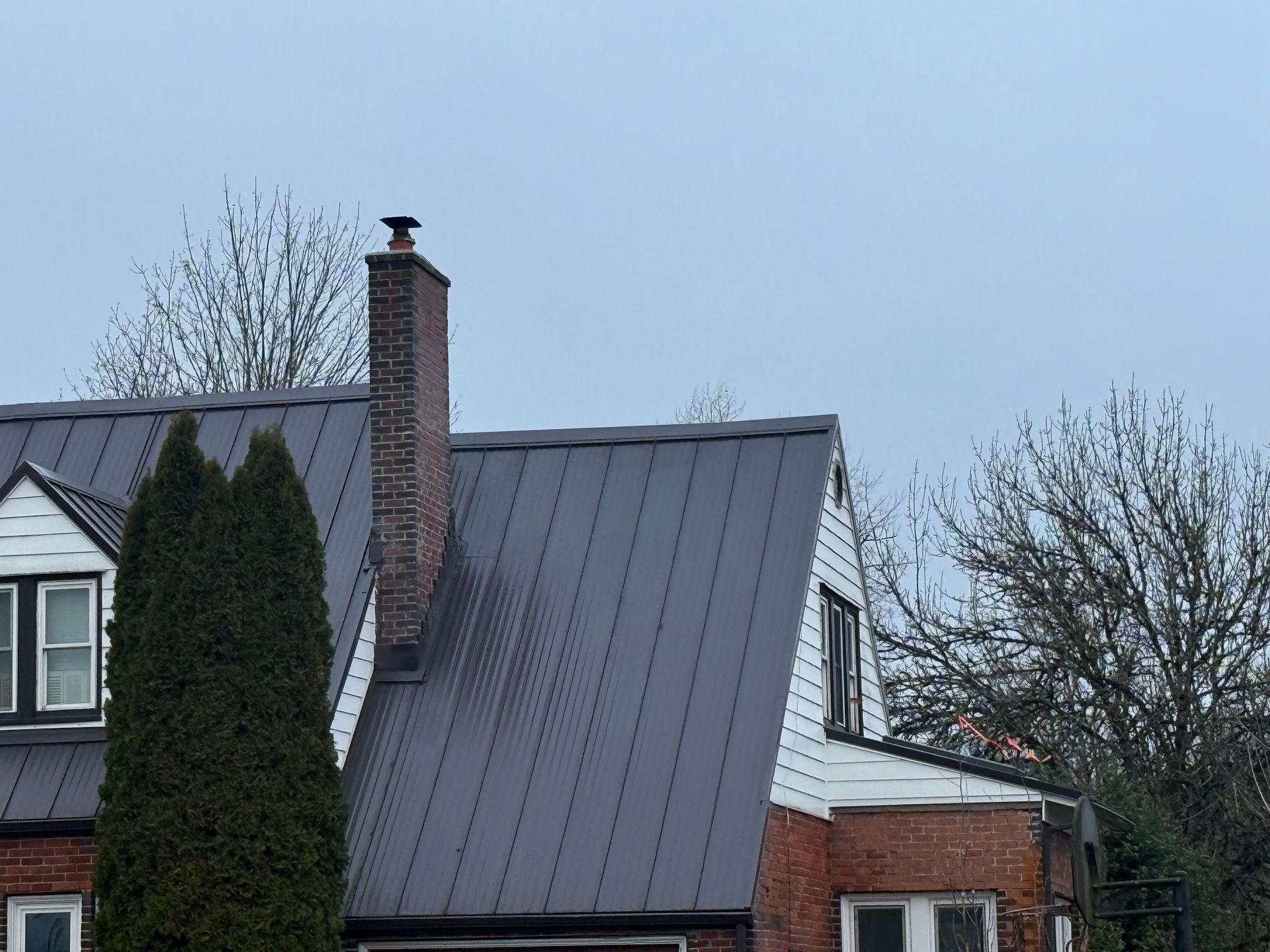 Brick house with dark metal roof and chimney under a cloudy sky