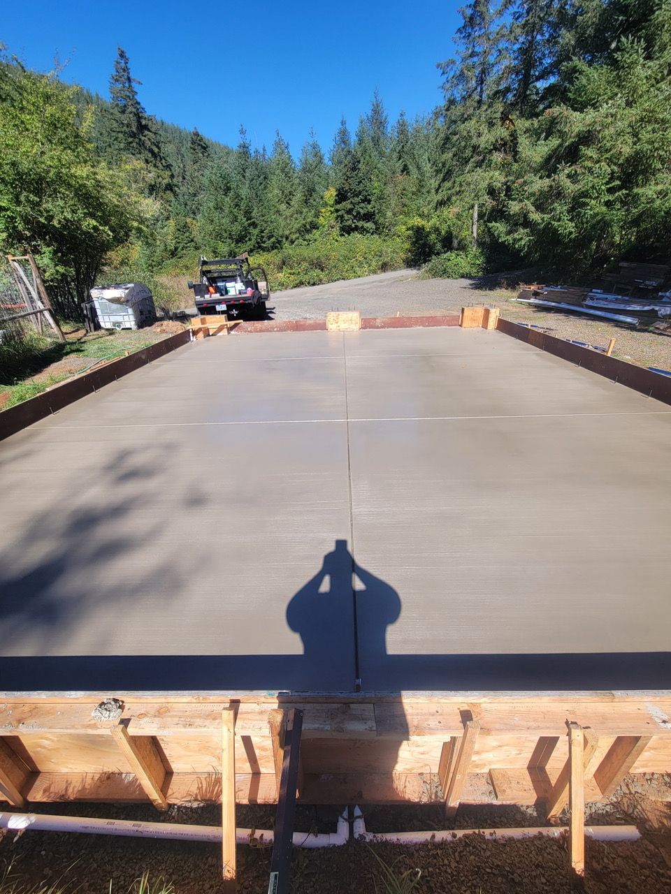Concrete driveway slab on wooden formwork at a wooded construction site, with an ATV and worker in the background