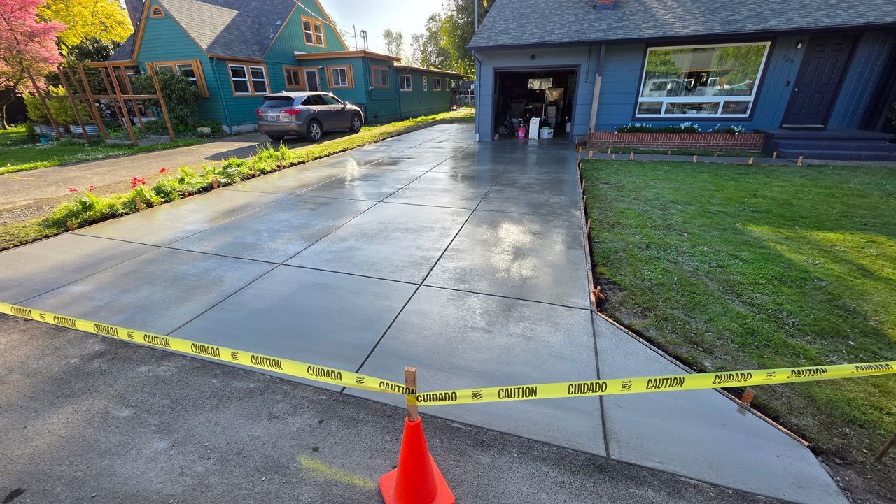 Driveway under construction, cordoned off with yellow caution tape and an orange cone in front of a house.