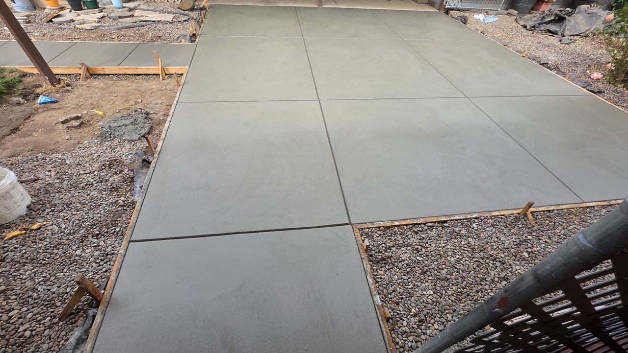 Freshly poured concrete walkway slabs beside gravel landscaping and a black metal railing