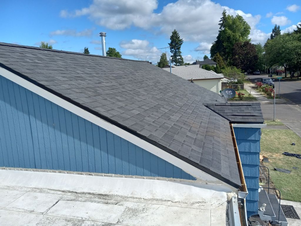 Blue-sided house with a gray shingle roof under a clear sky, viewed from above.