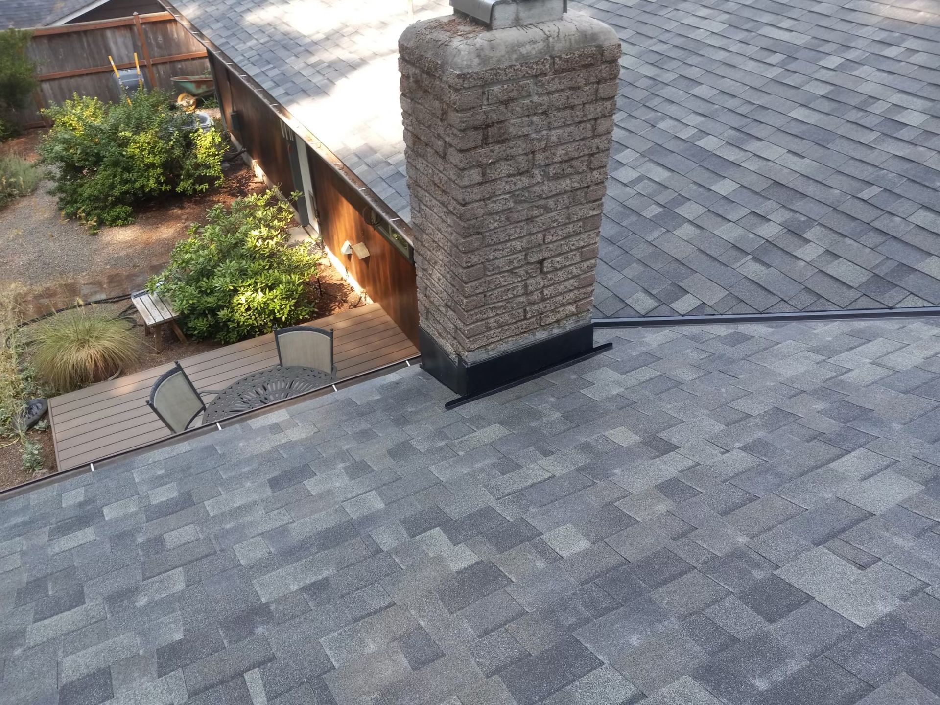 Rooftop with gray shingles and a brick chimney beside a landscaped yard and walkway