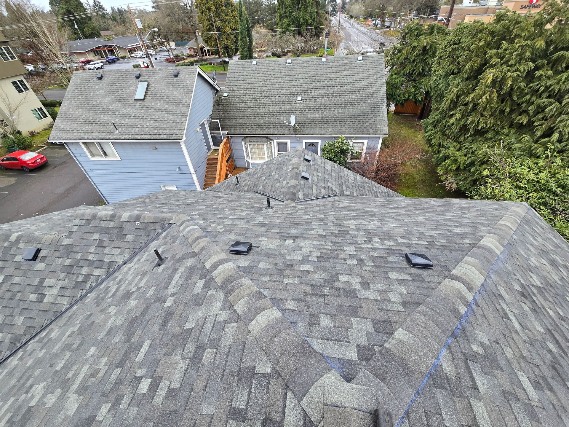 Overhead view of a gray asphalt shingle roof, with a view of nearby houses and a road.