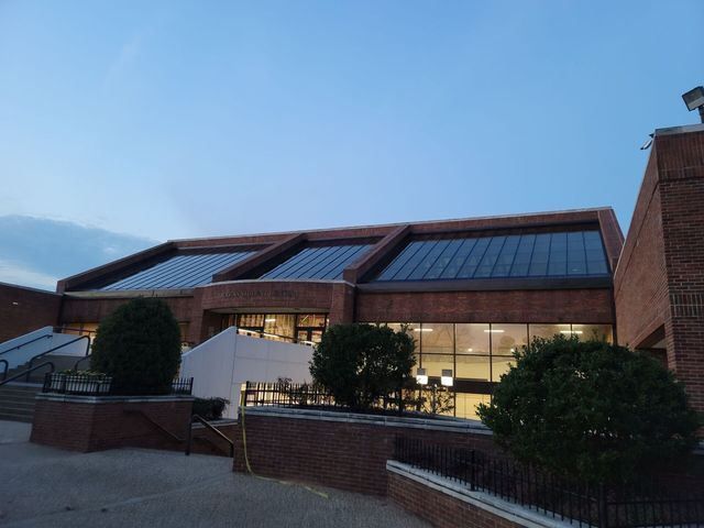 Brick building with large windows and a flat roof with skylights, under a blue sky.