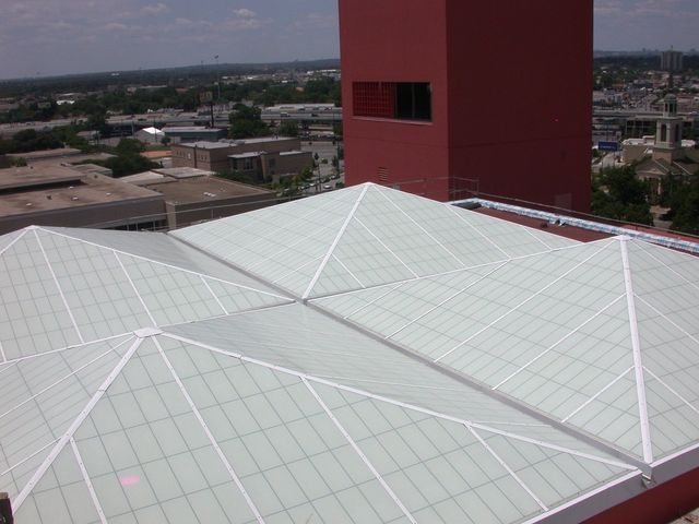 Glass roof with white frame, adjacent to a tall red building on a sunny day.