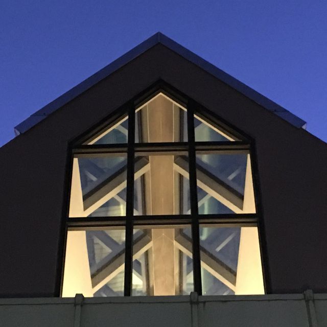 Triangular window with black frames illuminated from within against a dark blue sky.