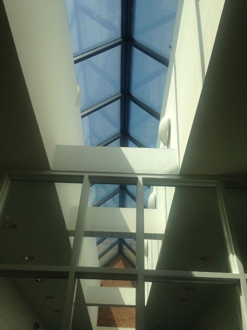 Skylight interior with a glass ceiling and white walls, allowing a view of the sky.