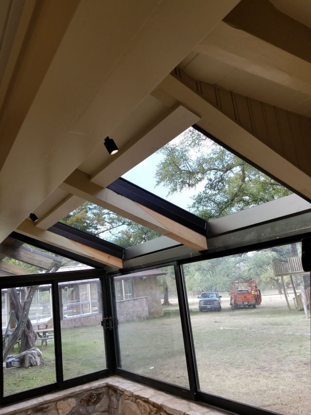Interior view of a room with angled glass windows and skylights, overlooking a grassy yard and trees.