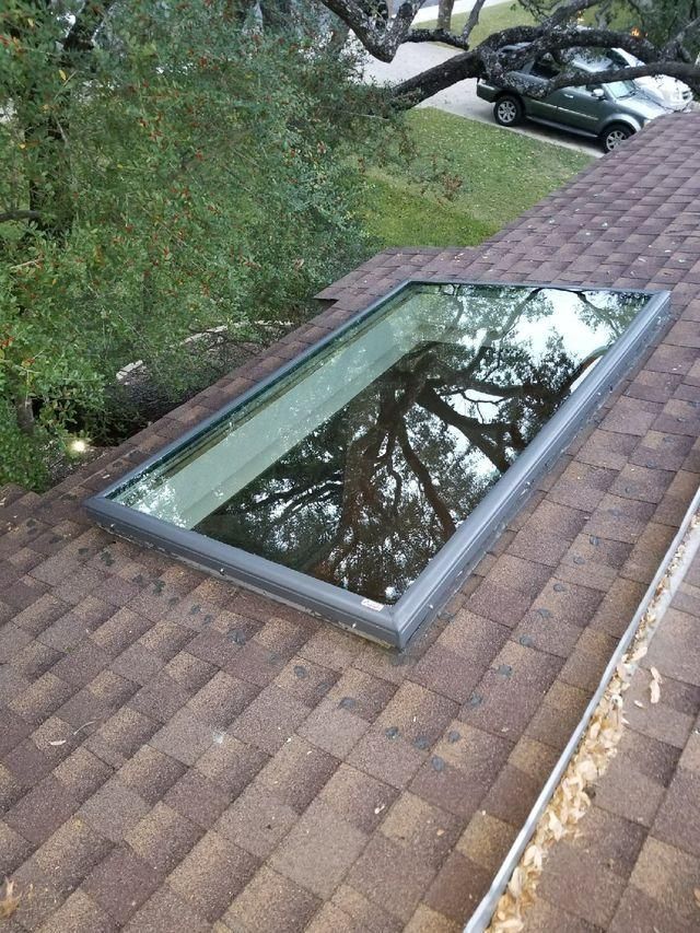 Rectangular skylight on a brown shingled roof, reflecting a tree.