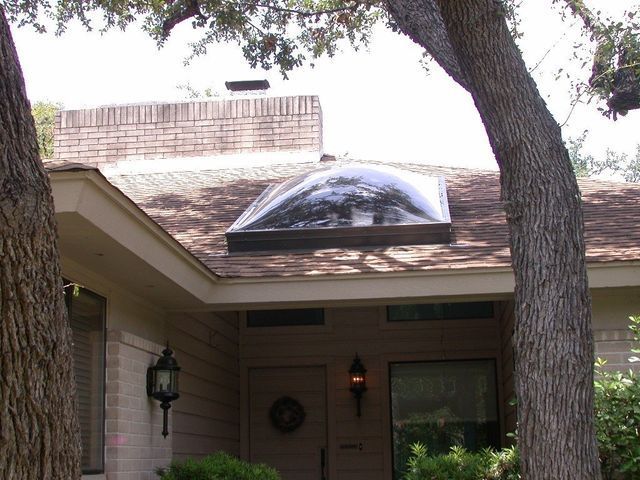 House exterior with a large dome-shaped skylight on the roof, flanked by trees and a brick chimney.