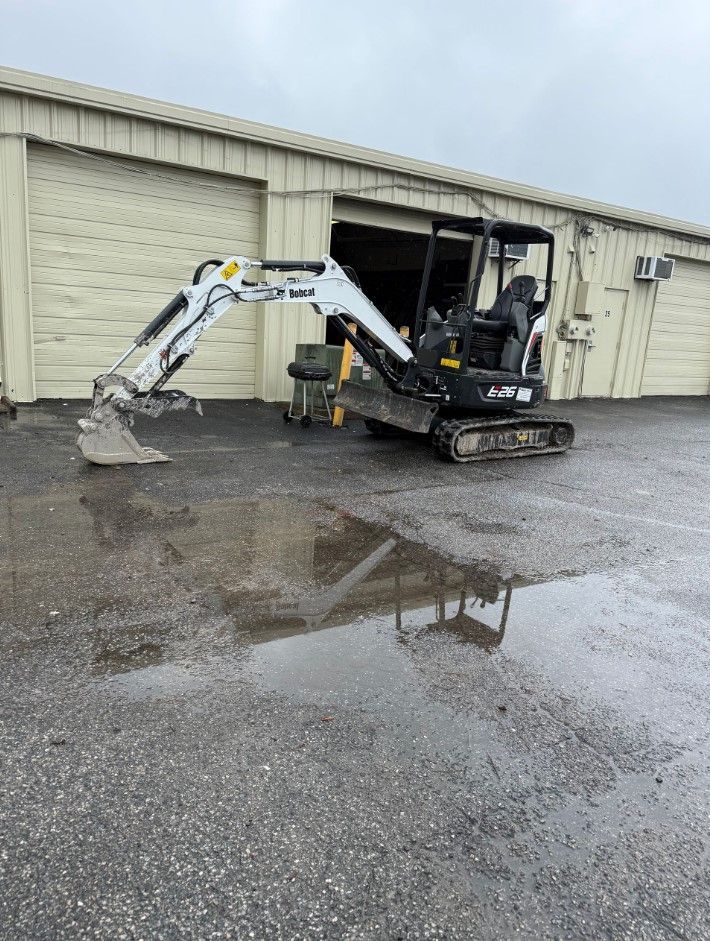 Mini excavator parked in front of a building with a large puddle reflecting the machine.