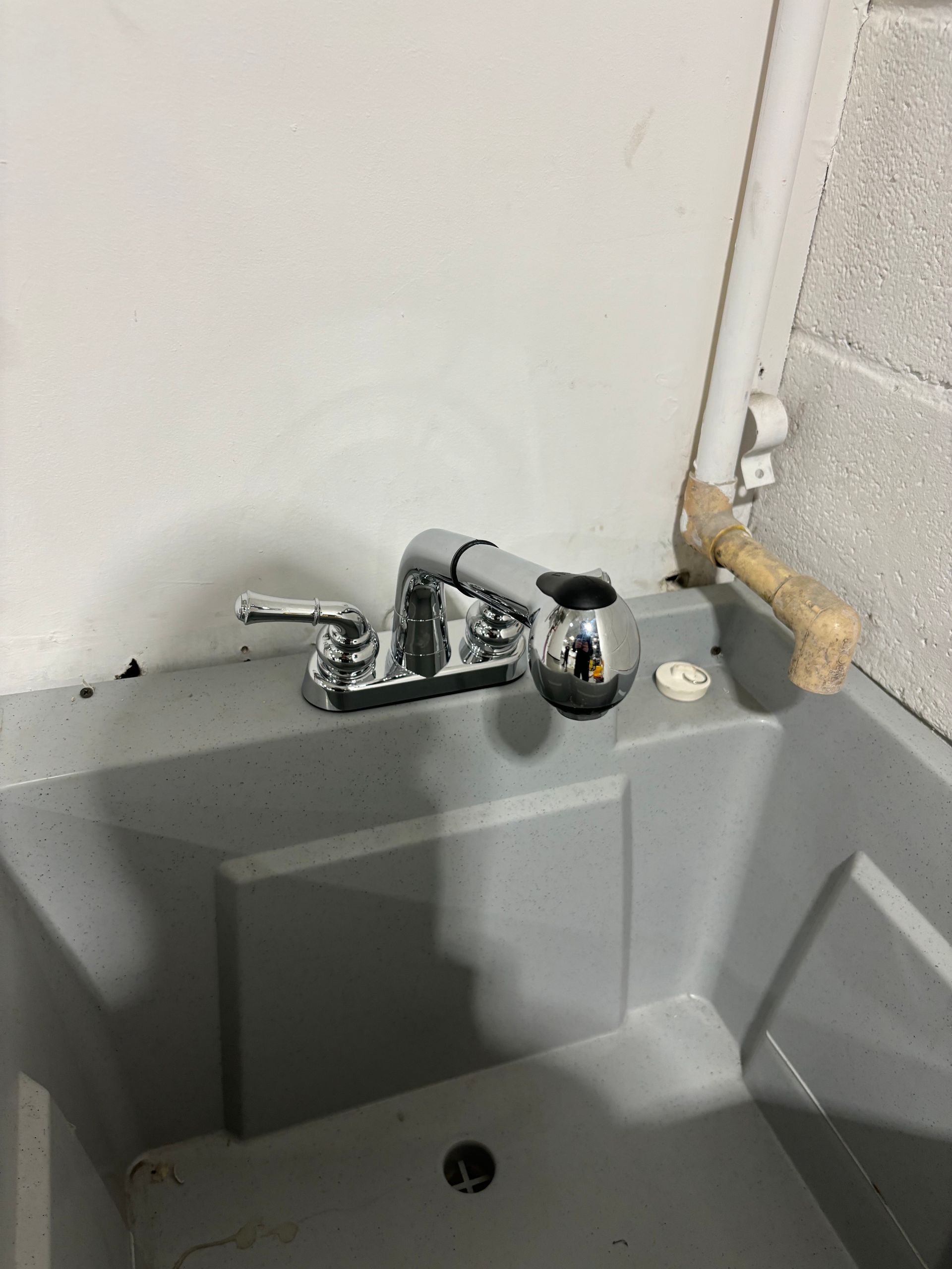 A utility sink with a chrome faucet and spray nozzle. The sink is grey and set against a white wall.