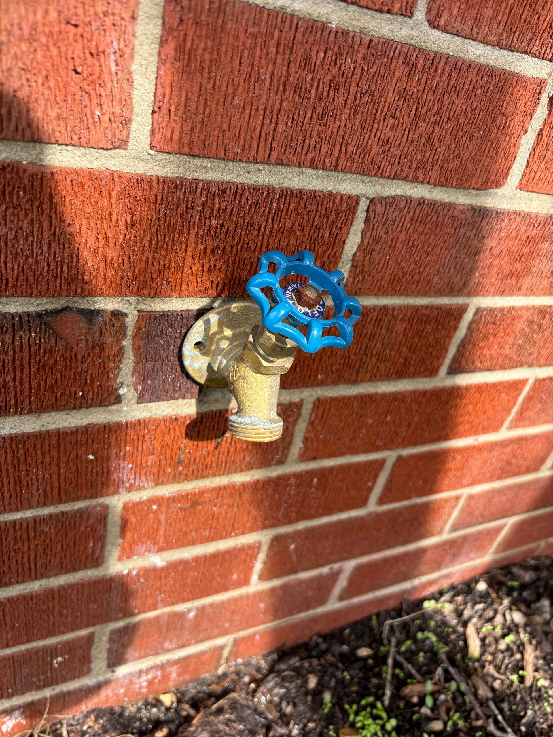 A brass spigot with a blue handle attached to a red brick wall.